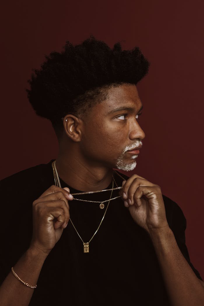 Portrait of a young man with necklaces against a red background.